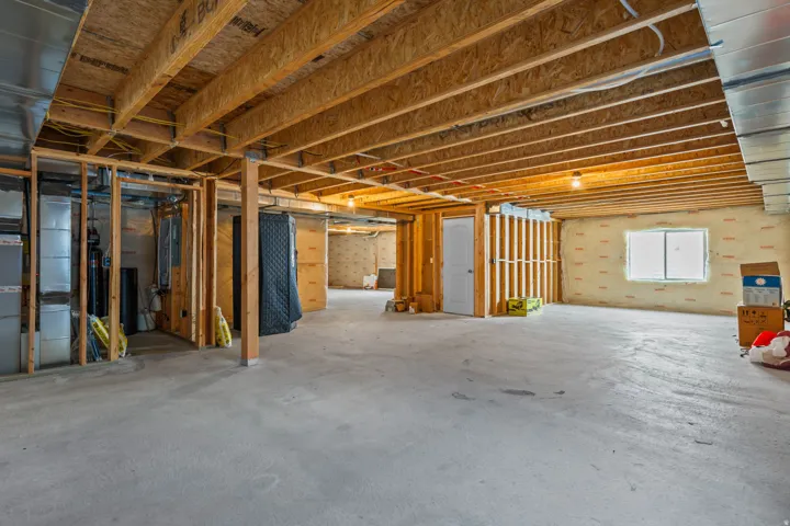 Unfinished basement with concrete flooring, exposed wood joists, framed interior walls, a window, and a white door
