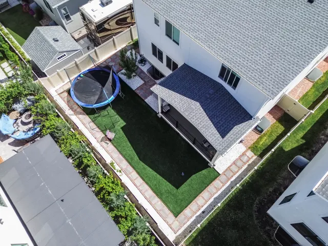 Turf lawn with surrounding paver stone pathway, covered patio, and privacy fencing