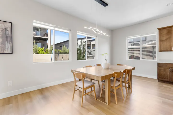 Light wood-finish flooring, white walls, multiple windows, built-in cabinetry, and a modern linear light fixture