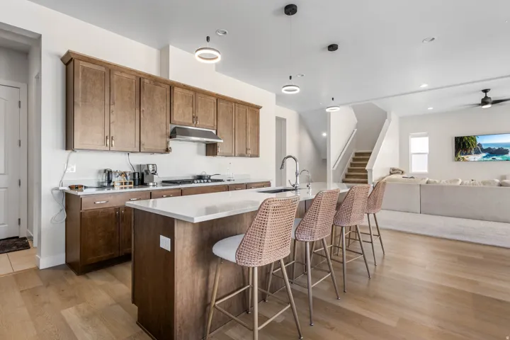 Modern kitchen featuring wood cabinetry, white countertops, a central island with an integrated sink, and wood-finish flooring