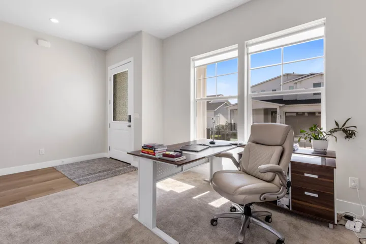 Recessed lighting, wood-finish flooring, white paneled door with frosted glass, two large windows, and neutral wall paint