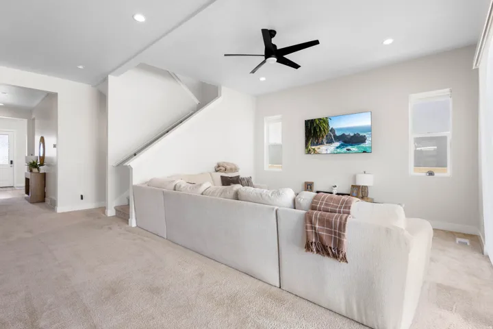 Recessed ceiling lighting, a modern ceiling fan, staircase with white railing, and carpeted flooring