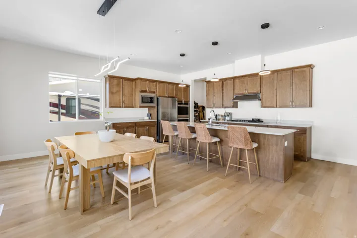 Open-concept living space featuring wood-finish flooring, a kitchen island with seating, stainless steel appliances, and a modern linear light fixture