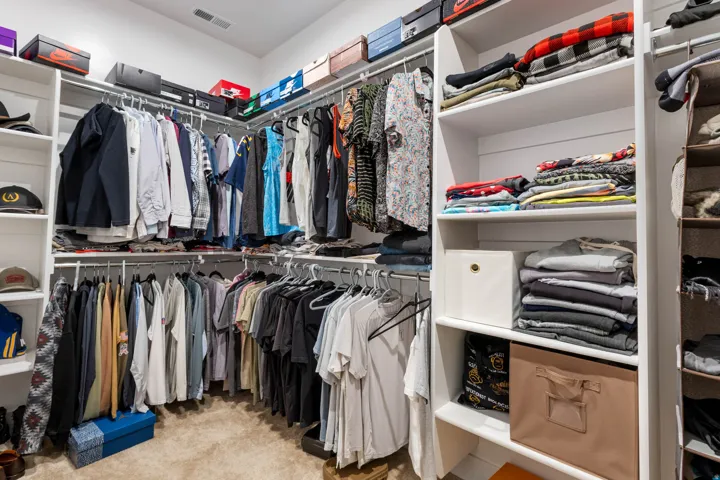 Walk-in closet with carpet flooring, white built-in shelving, and multiple hanging rods