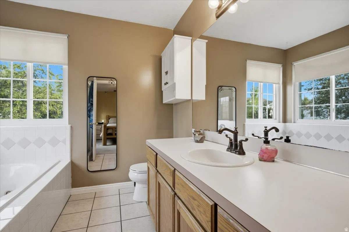Dual windows, integrated vanity with single basin, built-in tub, and tiled flooring