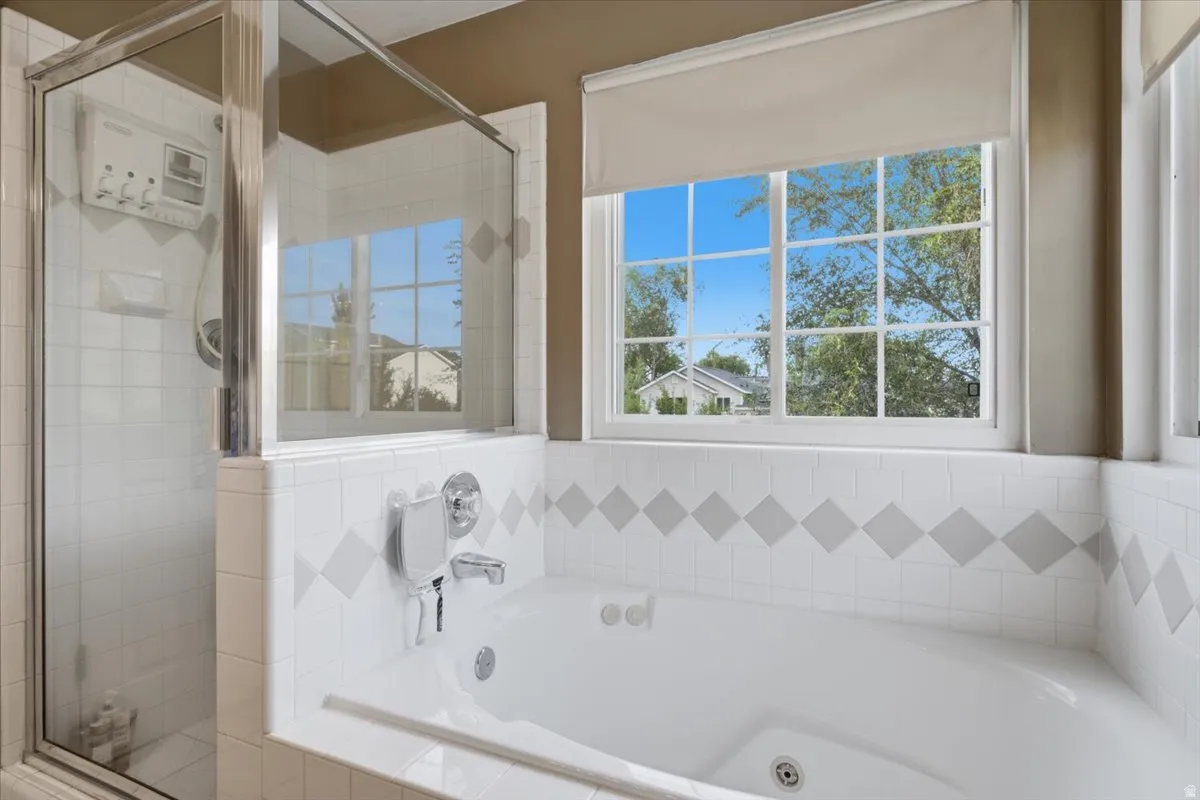 Master bathroom featuring a soaking tub with tile surround detailing, dual vanity with integrated sink, chrome fixtures, and a separate glass-enclosed shower enclosure