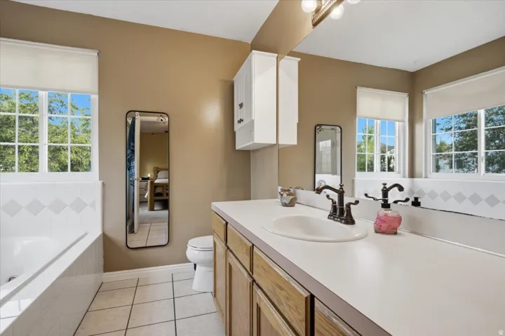 Dual windows, integrated vanity with single basin, built-in tub, and tiled flooring