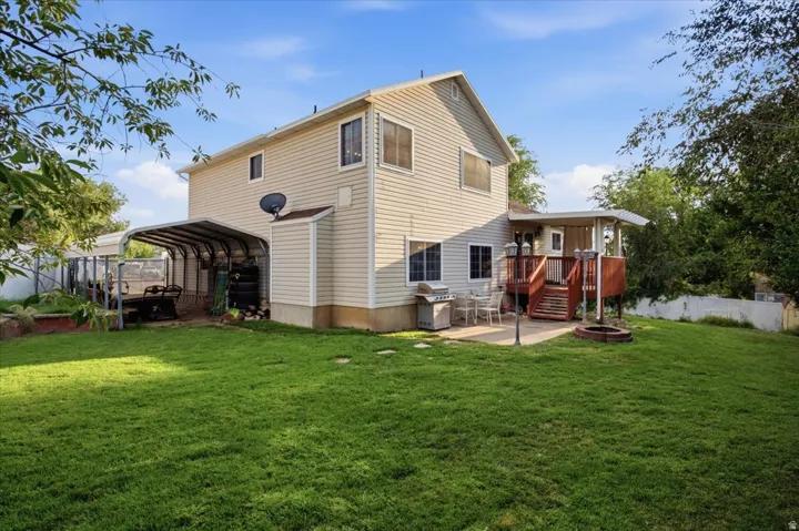 Expansive rear yard featuring a large patio, a raised wood deck, and a covered carport structure