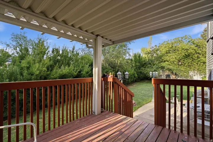 Covered deck with wood-finish decking and railings, overlooking a manicured lawn with mature trees and a concrete pathway