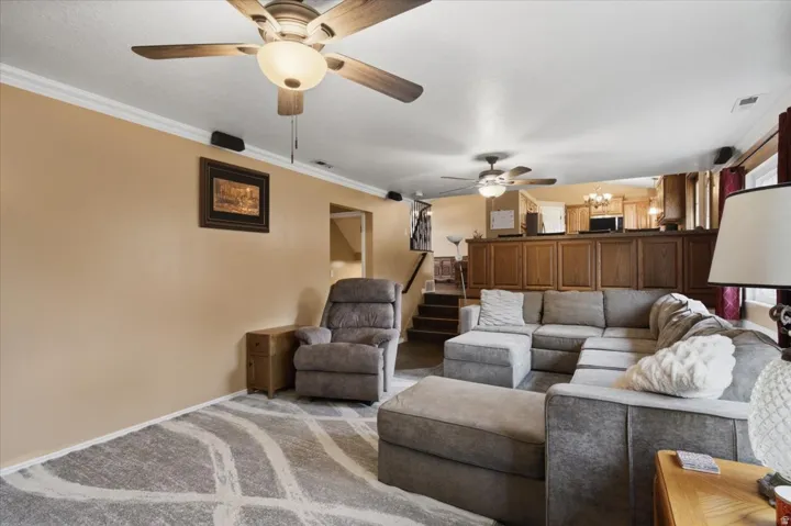 Spacious living area featuring a ceiling fan, crown molding, and wood-finish cabinetry