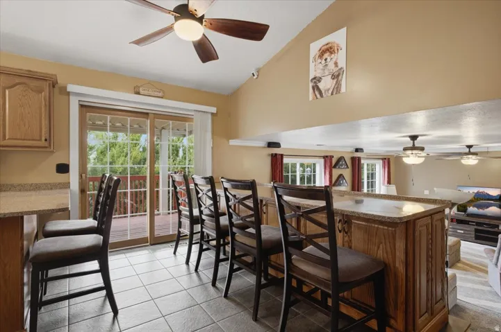 Bright kitchen and dining area featuring cream-colored walls, tile flooring, wood cabinetry with integrated countertop workspace, ceiling fan with integrated lighting, French doors opening to outdoor space, and stainless steel range hood
