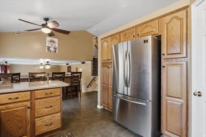Kitchen with wood-finish cabinetry, stainless steel refrigerator, and stone-finish countertops
