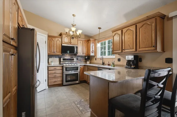 Kitchen with wood cabinetry, stainless steel appliances, a tile backsplash, and a breakfast bar with a granite-style countertop