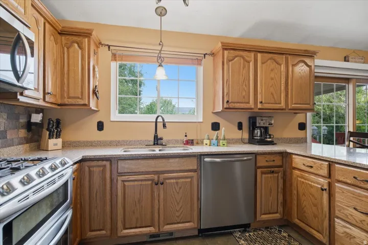 Kitchen featuring wood cabinetry, stone-finish countertops, stainless steel appliances, and a tiled backsplash
