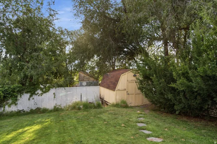 Mature landscaping with established trees and lush lawn space, complemented by a storage structure and white perimeter fencing