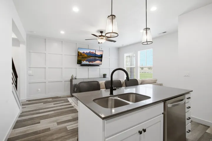 Modern kitchen featuring stainless steel dual basin sink with integrated cooktop, white cabinetry with hardware accents, wood-finish plank flooring, and pendant lighting