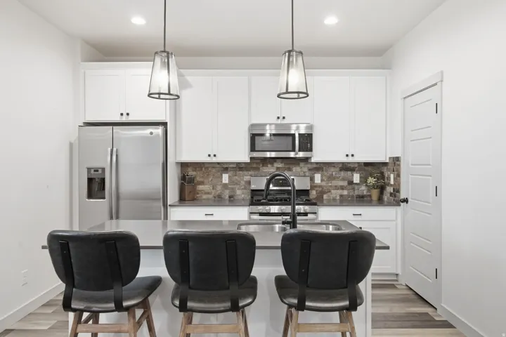 Kitchen featuring stainless steel appliances, white cabinetry, an island with an integrated sink, and wood-finish flooring