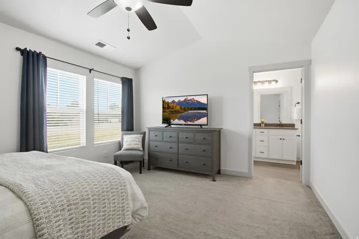 Vaulted ceiling with a ceiling fan, dual windows with blinds, plush carpet flooring, and an en suite bathroom featuring a dual vanity with a large mirror