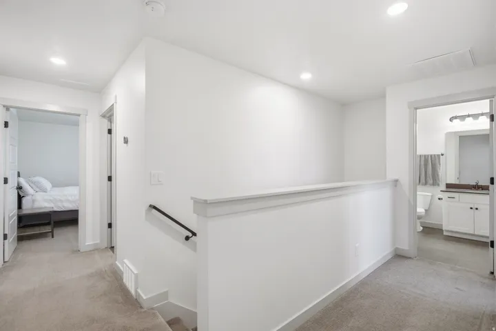 Carpeted hallway with white walls, recessed lighting, and a white banister with a black handrail
