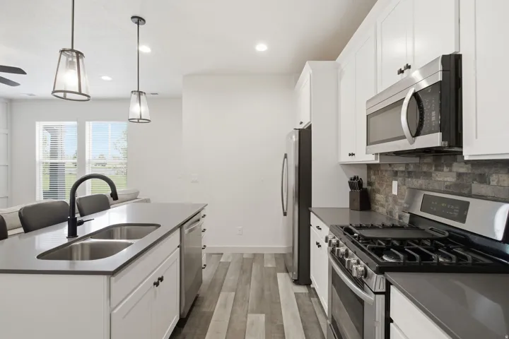 Contemporary kitchen featuring white cabinetry, stainless steel appliances, dark countertops, and wood-finish flooring