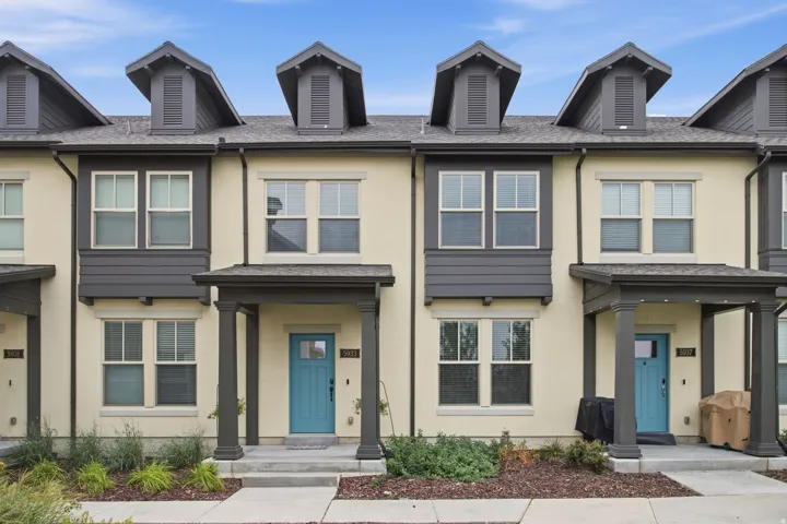 Stucco exterior featuring dormer windows, covered entryways, blue entry doors, and ground-level plantings