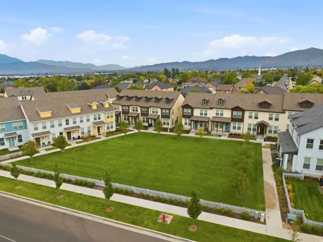 Residential community featuring multi-story townhomes with dormer windows, a large central green space, and mountain scenery in the distance
