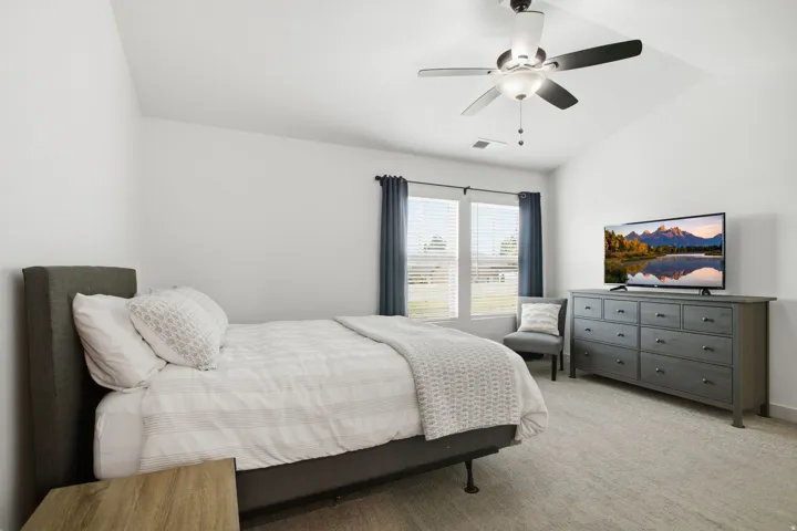 Vaulted ceiling with a ceiling fan, two large windows with blinds, and carpeted flooring