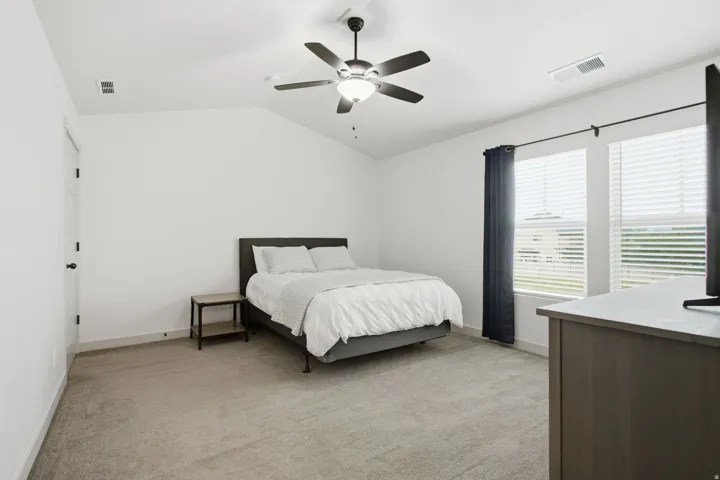 Vaulted ceiling with a ceiling fan, carpeted flooring, and a pair of windows with blinds