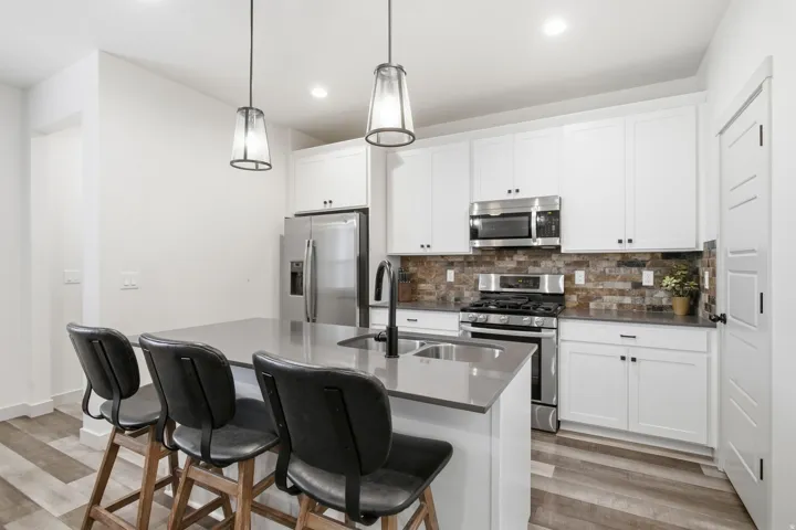 Kitchen featuring a center island with sink, stainless steel appliances, white cabinetry, a tiled backsplash, and recessed lighting