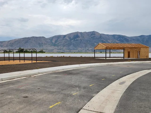 Newly constructed covered pavilion with mountain backdrop, asphalt road, and concrete sidewalk
