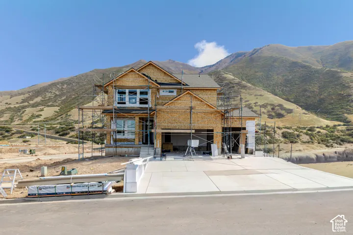 New construction frame featuring a multi-level wood-clad exterior, asphalt shingle roofing, and a paved concrete driveway against a mountain backdrop