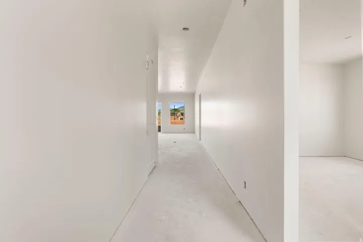 Long hallway with light-colored walls and flooring, featuring two windows providing exterior scenery