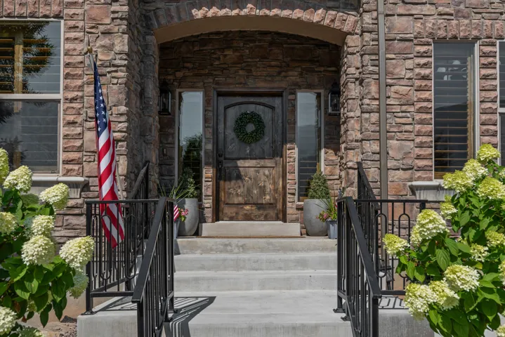 Stone facade, arched entryway, dark wood front door, decorative sidelights, and concrete steps with black railings