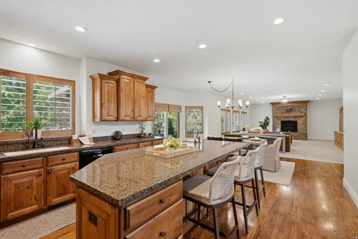 Kitchen island with bar seating, wood-finish cabinetry, granite countertops, and recessed lighting