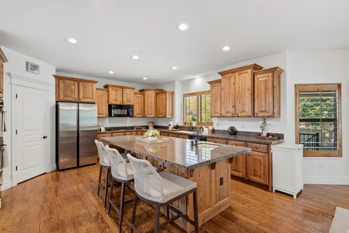 Kitchen featuring wood-finish flooring, recessed lighting, wood cabinetry, stone countertops, and a stainless steel refrigerator