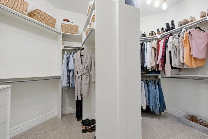 Walk-in closet with carpet flooring, white built-in shelving, and multiple clothing rods
