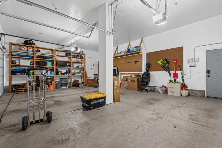 Spacious garage with concrete flooring, overhead garage door system, built-in wooden shelving, and a secondary entry door