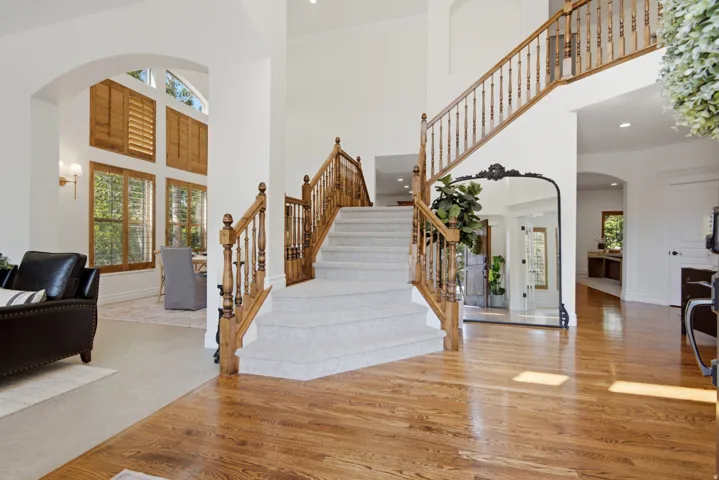Hardwood flooring, arched entryway, custom wood shutters, carpeted staircase with wood banister, and recessed lighting