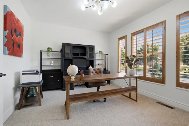 Recessed lighting, wood-finish desk, carpeted flooring, and multiple windows with wood-finish plantation shutters