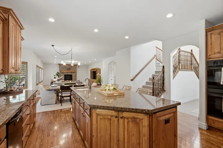 Open-concept living space with wood-finish flooring, a stone-surround fireplace, and a kitchen island featuring a sink and seating