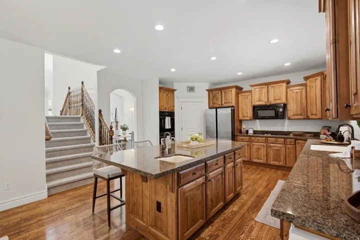 Kitchen featuring rich wood cabinetry, stone countertops, stainless steel refrigerator, black microwave, and wood-finish flooring
