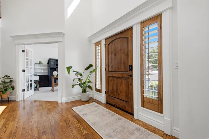 Arched wood-panel entry door, wood-finish flooring, sidelight windows with plantation shutters, double French doors, and vaulted ceilings