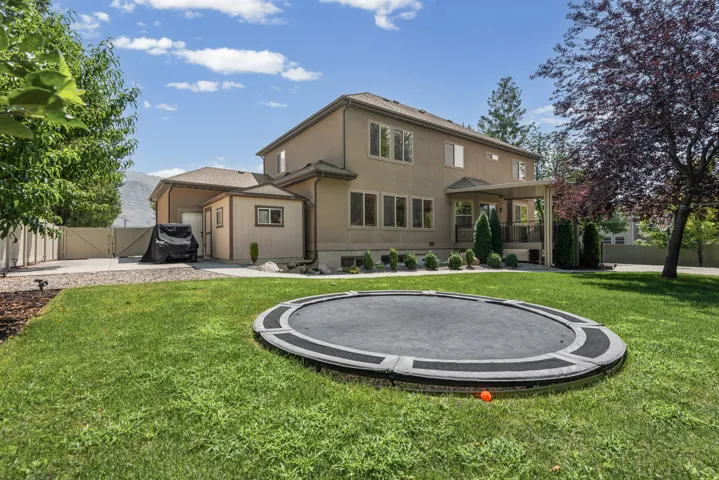 Expansive rear yard featuring green lawn, mature trees, and a covered patio