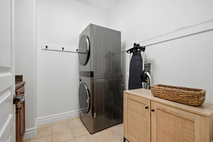 Laundry area featuring stacked appliances, tile flooring, and a built-in hanging rack