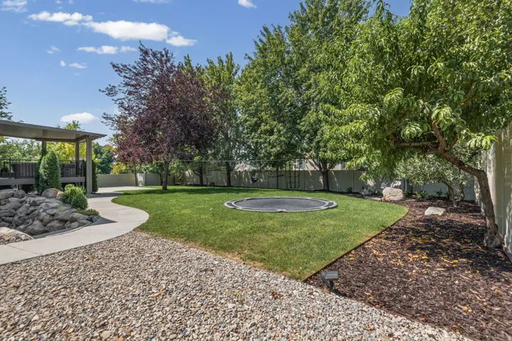 Expansive backyard featuring a manicured lawn, mature trees, and a covered deck