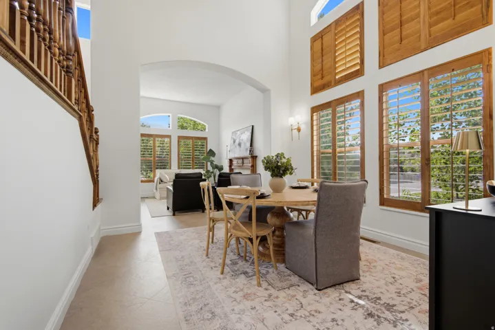 Two-story windows with wood shutters, arched entryway, high ceilings, and a wood-finish staircase with ornate balusters
