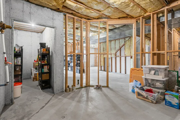 Unfinished basement space featuring concrete walls, exposed ceiling joists with insulation, concrete flooring, and wood framing