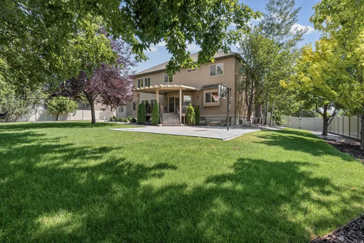Expansive green lawn with mature trees, a concrete patio, and a covered pergola