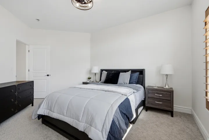Neutral wall paint, light-toned carpet flooring, ceiling fan, white paneled door, and plantation shutters