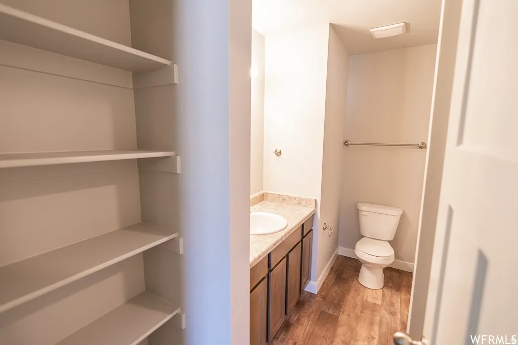 Built-in shelving, wood-finish flooring, vanity with integrated sink, and a commode
